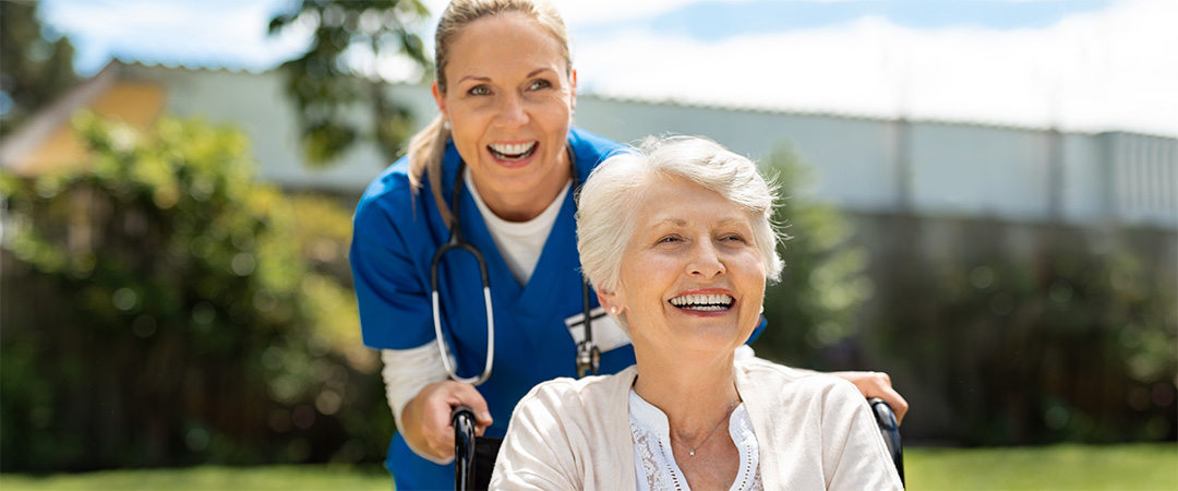 Nurse smiling and pushing a patient outside in her wheelchair